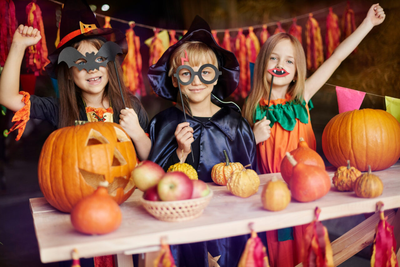 Kids wearing costumes and holding Jack-o'-lanterns ready to trick-or-treat at halloween.